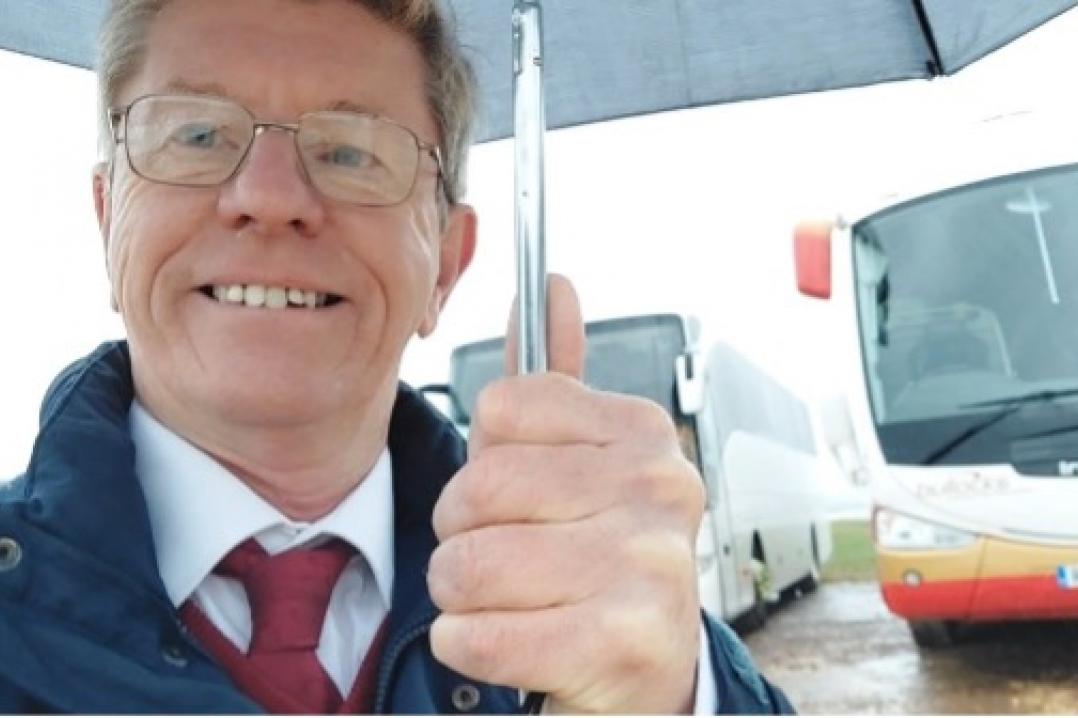 Graham under an umbrella infront of a bus